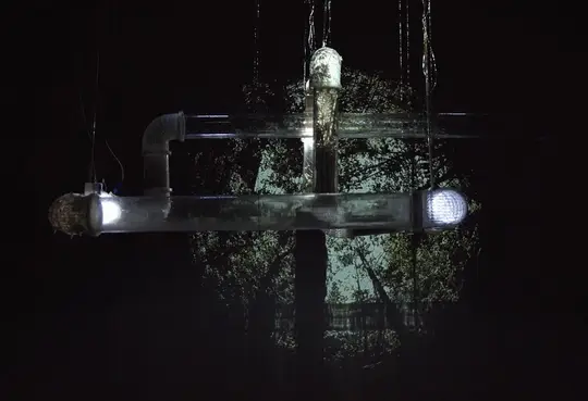 Transparent pipes suspended in the dark, lit at both ends, in front of a circular projection of trees